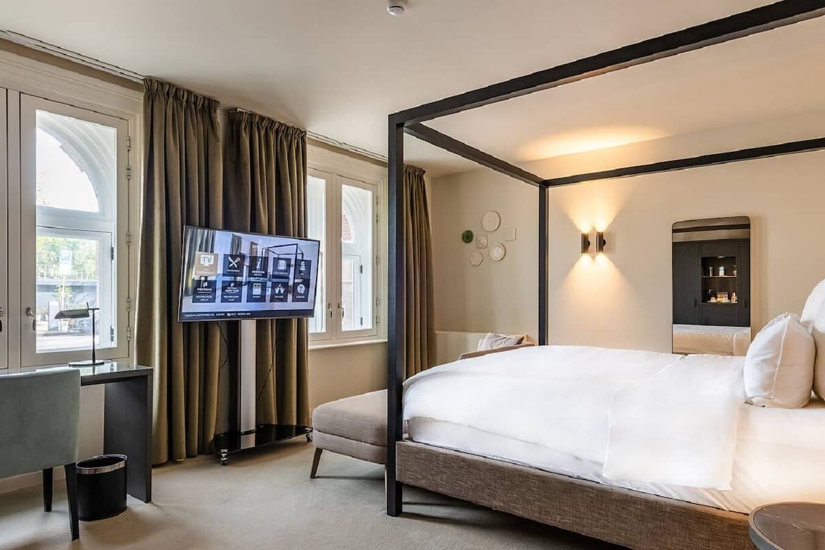 A four-poster bed, a flat-screen TV, and a desk with a lamp in a hotel room.