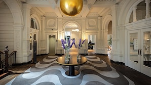 A grand lobby with a central round table, a reception desk, and a large gold spherical light fixture. - Pestana Amsterdam Riverside (Amsterdam)