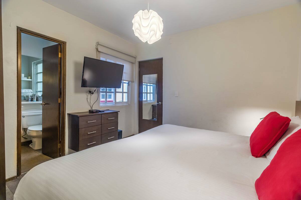 Une chambre dotée d’un grand lit, d’une commode, d’un téléviseur à écran plat et d’un luminaire moderne.