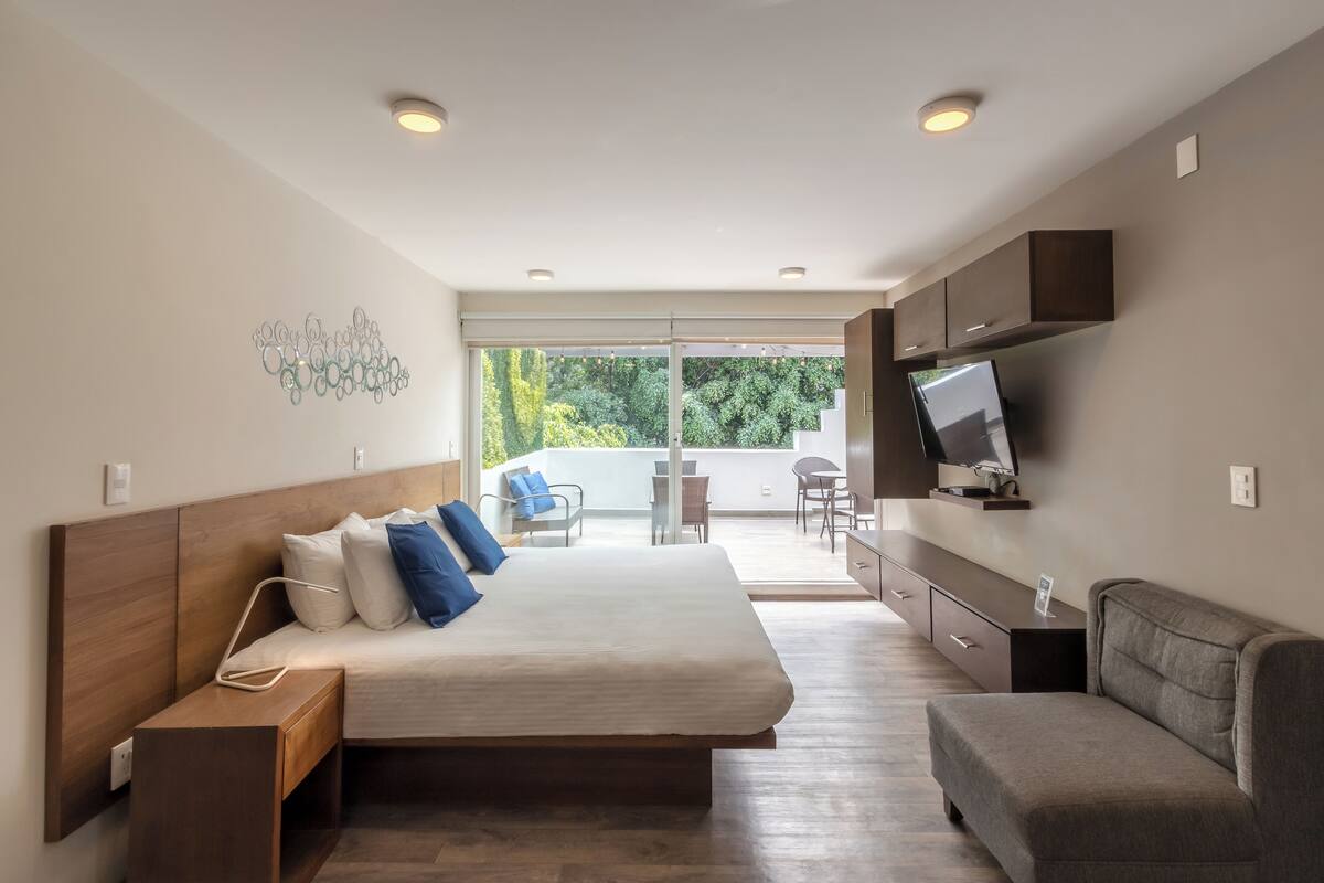 Une chambre moderne avec un grand lit, un téléviseur fixé au mur et un balcon avec un coin salon extérieur.