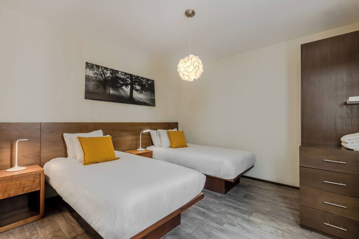 Une chambre d’hôtel avec deux lits, une armoire en bois, une table de chevet avec une lampe et un tableau accroché au mur.