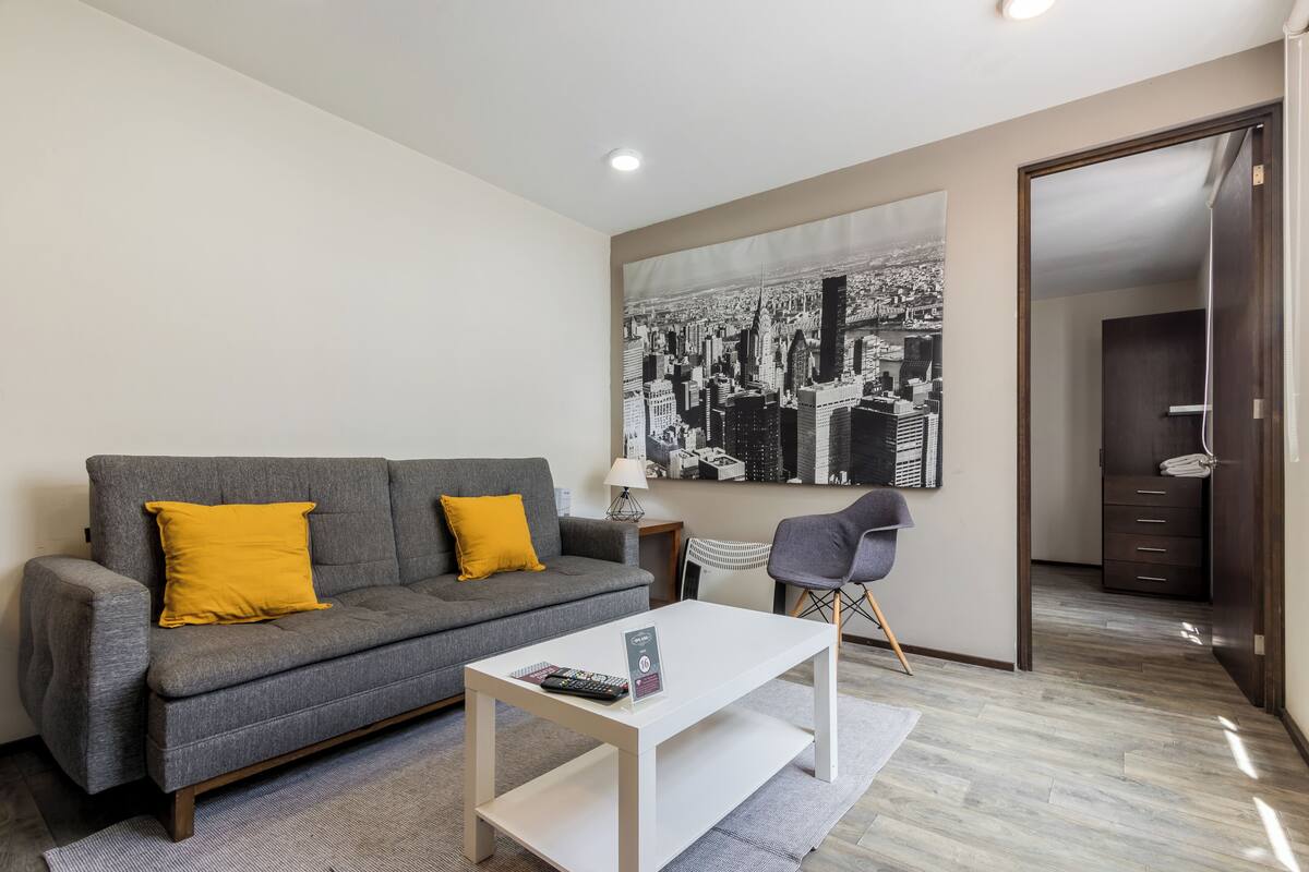 Un salon moderne avec un canapé gris, une table basse blanche et un grand tableau représentant un paysage urbain en noir et blanc accroché au mur.