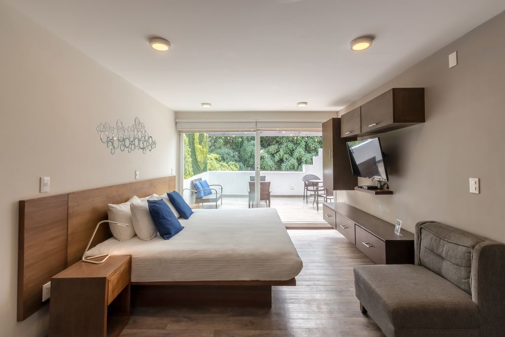 A modern bedroom with a large bed, a TV mounted on the wall, and a balcony with outdoor furniture.
