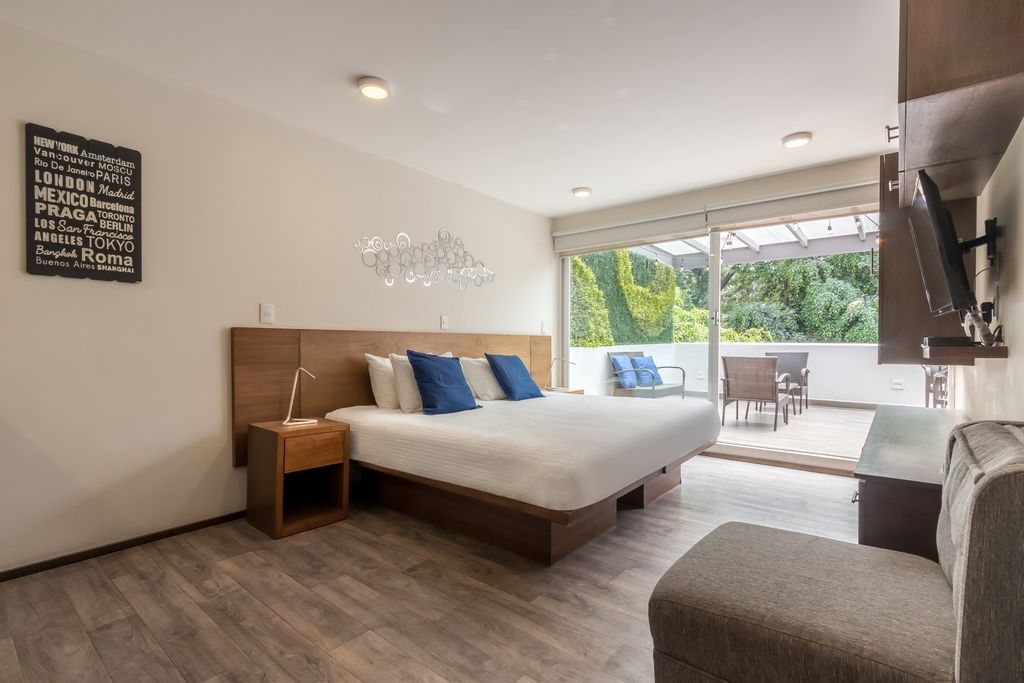 Une chambre moderne avec un grand lit, une table de chevet, une chaise et une vue sur l’extérieur grâce à une porte vitrée.