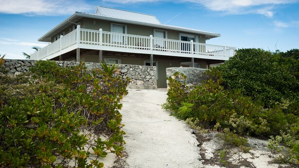 A beachfront property with a balcony, a stone wall, and a pathway leading to the entrance. - Caribbean Sea Breeze Villas (Providenciales)