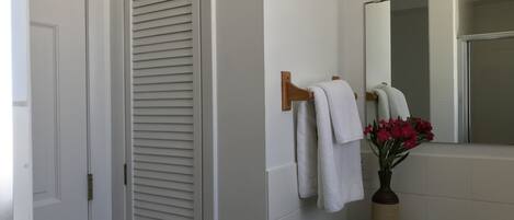 Une salle de bain avec une porte blanche, un porte-serviettes avec deux serviettes blanches, un miroir, un vase avec des fleurs rouges et des articles de toilette sur le comptoir.