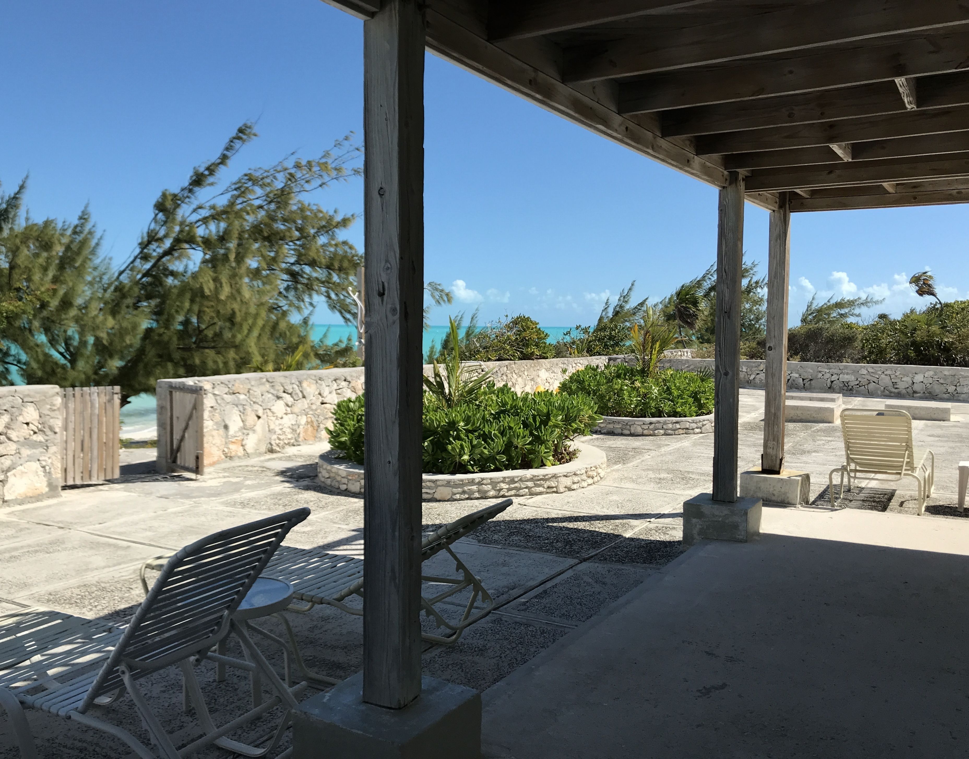 An outdoor patio area with a wooden pergola, seating arrangements, and a view of the ocean.