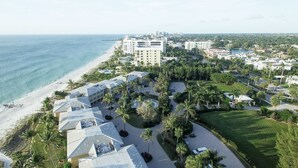 Vista aérea de un complejo turístico frente al mar, con varios edificios, una playa y palmeras.