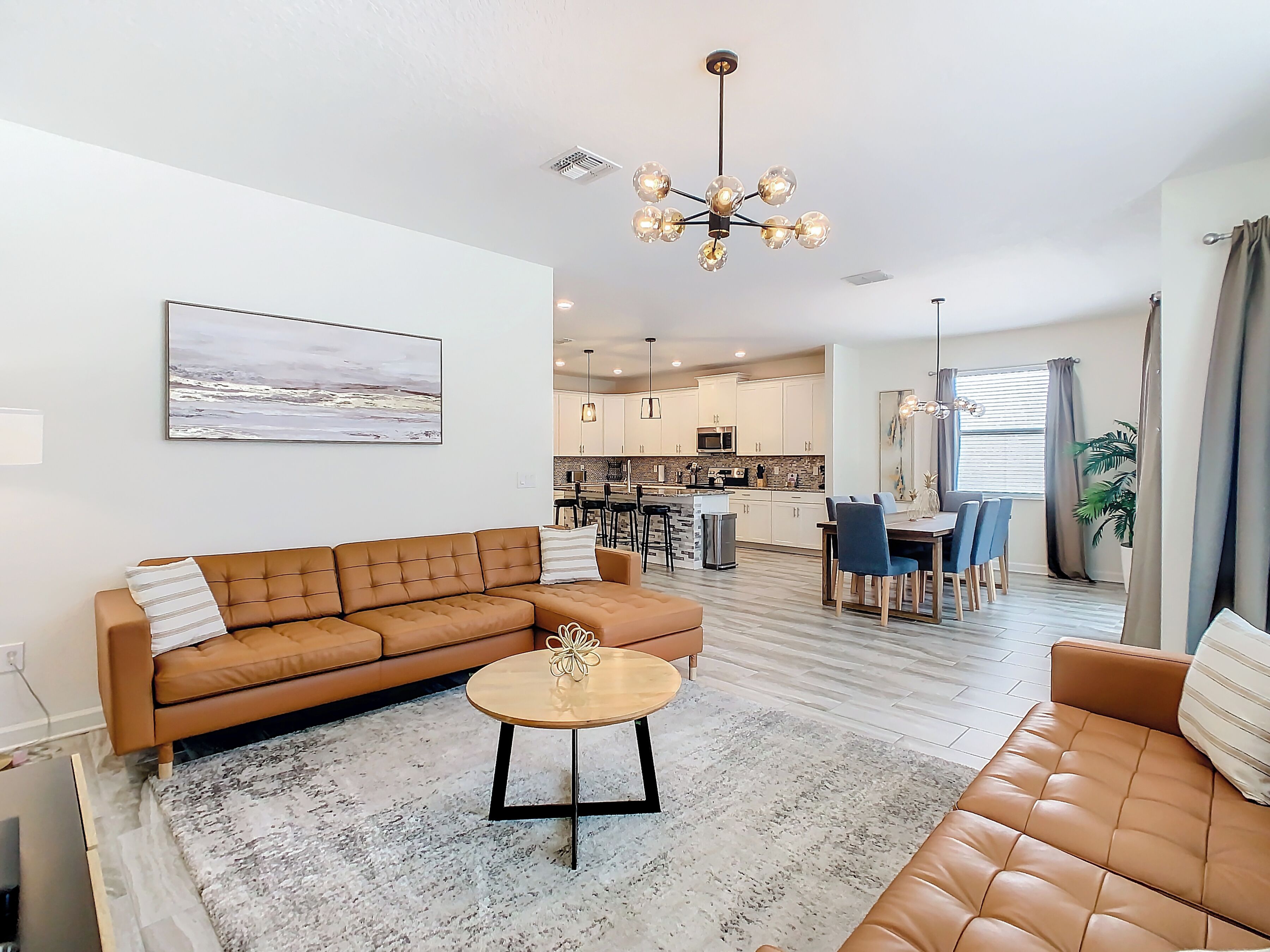 A modern living room with a brown leather sofa, a coffee table, and a dining area with a table and chairs.