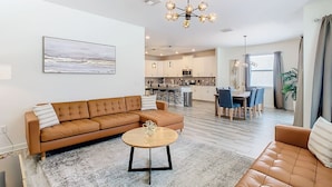 A modern living room with a brown leather sofa, a coffee table, and a dining area with a table and chairs. - 🏝️ 7BR/5BA Home w/ Private Pool & Spa, Themed Kids’ Rooms & Resort Fun | Storey Lake Near Disney (Kissimmee)