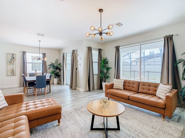 A spacious living room with a brown leather sofa, a round coffee table, and a dining area with a table and chairs.