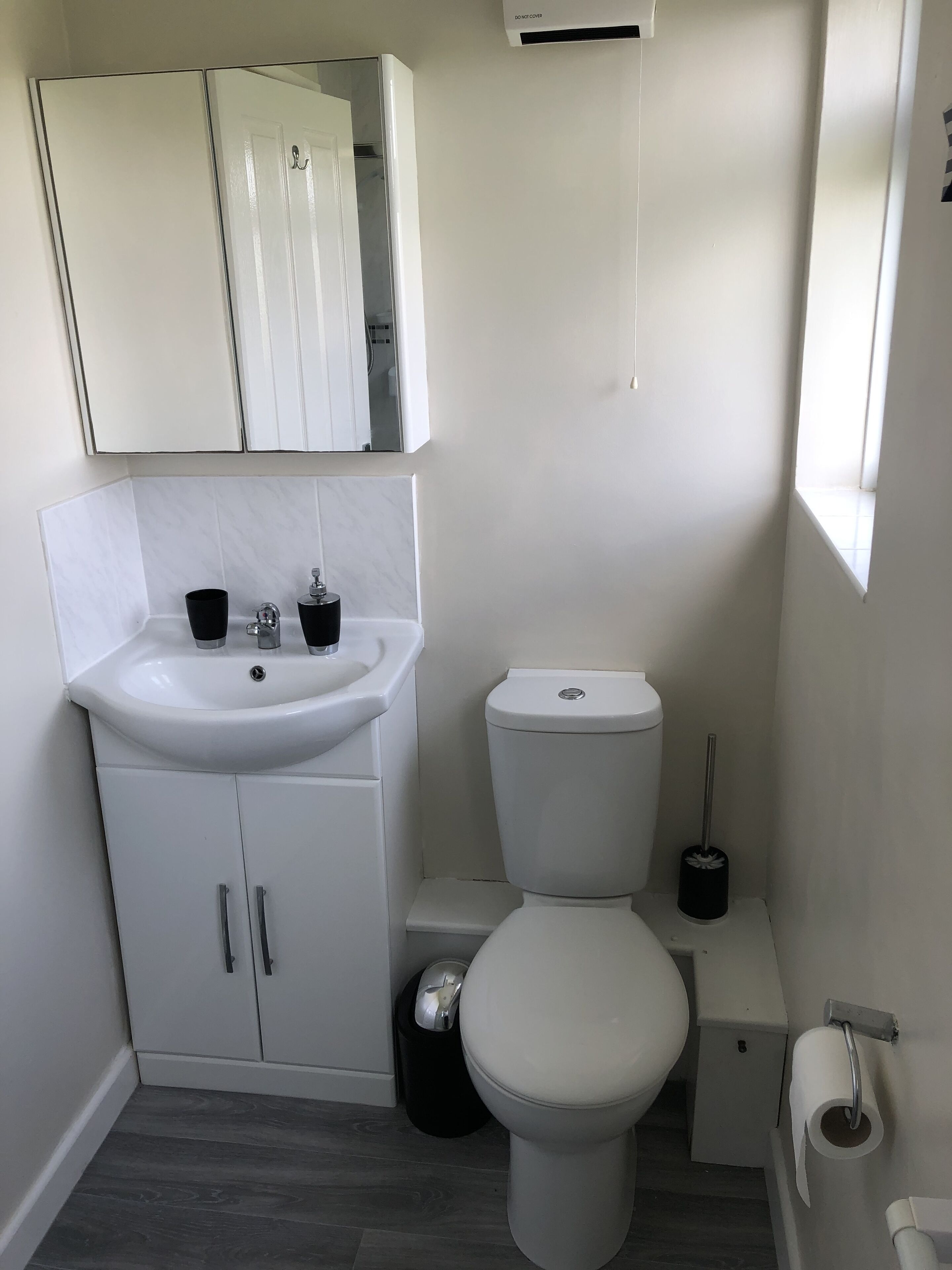 A small, modern bathroom with a white sink, toilet, and mirror.