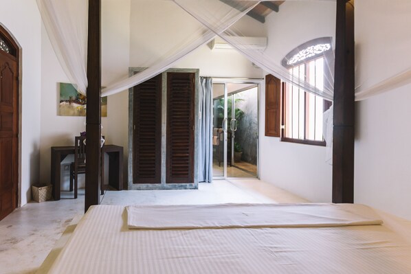 A bedroom with a bed, a chair, a table, and a window.