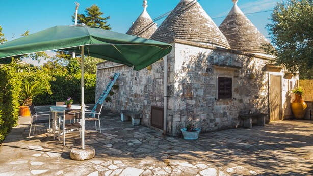 A stone building with conical roofs, a covered patio with outdoor furniture, and a staircase leading to an upper level. - Trullo la Chianca Homerelax (Locorotondo)