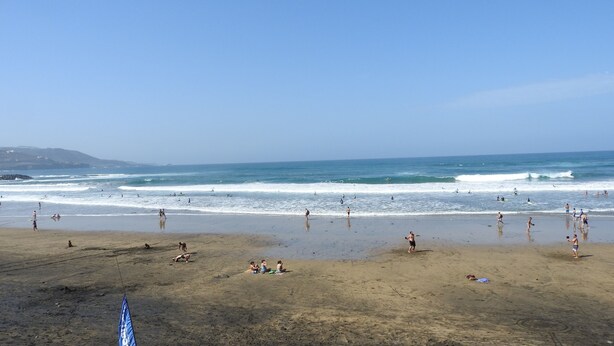 A beach with people swimming and walking along the shore.