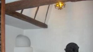 A room with a wooden ceiling, a stone fireplace, and two upholstered chairs.