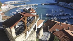 Un port de plaisance situé sur la côte, avec des bateaux amarrés, un mur de pierre et des bâtiments aux toits recouverts de tuiles rouges.