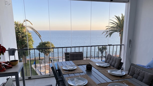 Un balcon avec une table à manger dressée pour quatre personnes, donnant sur une plage et la mer.