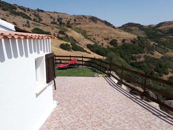 Une terrasse avec un sol carrelé, un fauteuil rouge et une clôture en bois donnant sur un paysage vallonné.