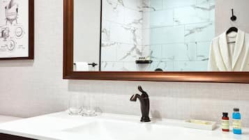 A bathroom with a marble backsplash, a large mirror, a modern faucet, and toiletries on the counter.