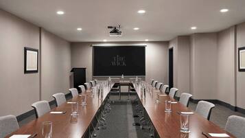 Uma sala de conferências com uma mesa comprida, cadeiras, um projetor e uma tela exibindo "THE WICK".