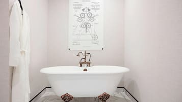 A bathroom with a freestanding bathtub, a white robe hanging on a hook, and a patent drawing on the wall.
