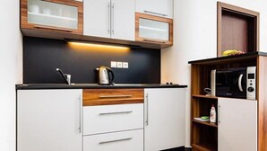 A modern kitchen with white cabinets, wooden accents, a black countertop, and a microwave. - Apartmánový dom Família Smokovec (Vysoké Tatry)