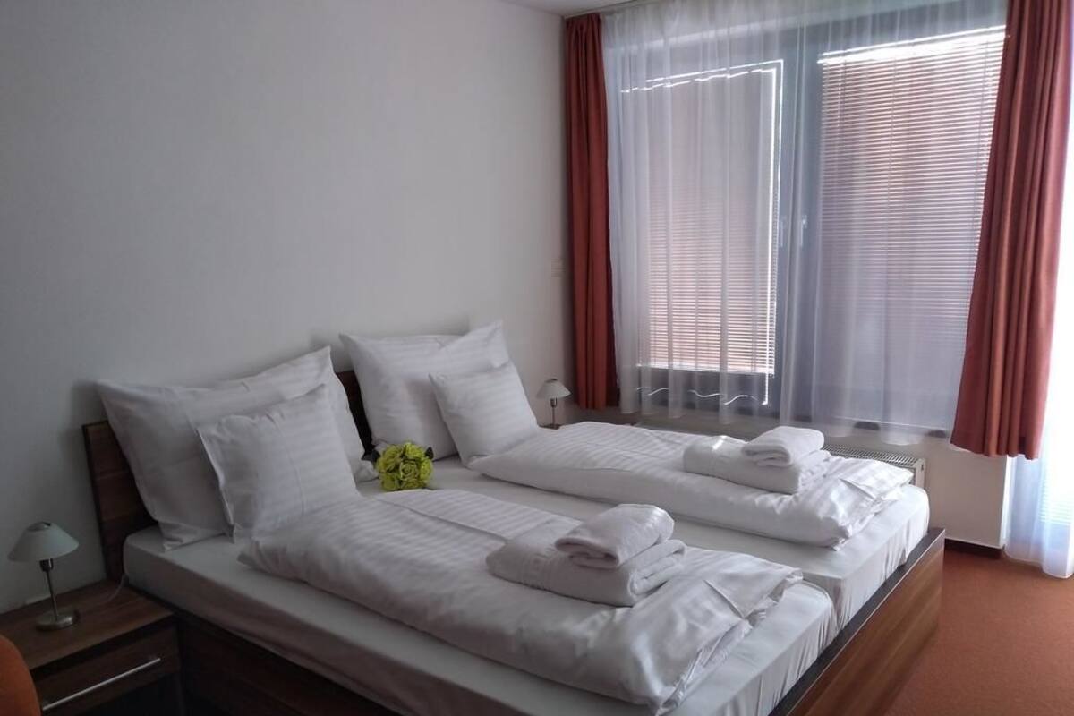 Un lit double avec du linge de lit blanc, une table de chevet avec une lampe et une fenêtre avec des rideaux.