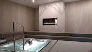 A modern spa area with a glass-enclosed hot tub, a metal bench, and a fireplace. - Apartmánový dom Família Smokovec (Vysoké Tatry)
