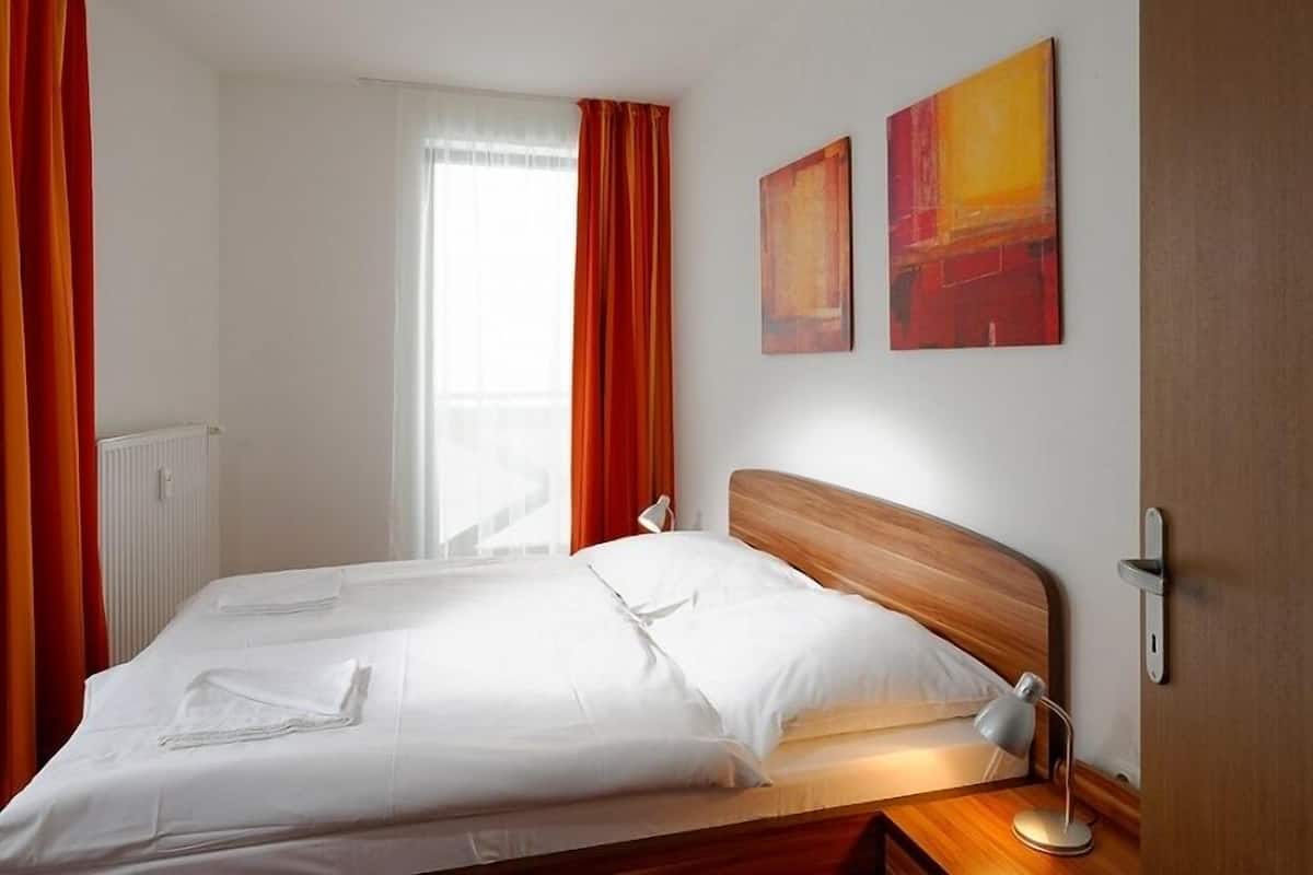 Une chambre d’hôtel avec un lit double, deux tableaux au mur, une lampe de chevet et une fenêtre avec des rideaux.