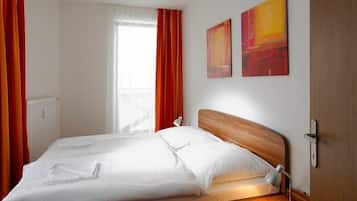 A hotel room with a double bed, two paintings on the wall, a bedside lamp, and a window with curtains.