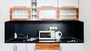 Una cucina moderna con mobili bianchi, elementi in legno, un piano di lavoro nero, un forno a microonde, un bollitore e un lavello.