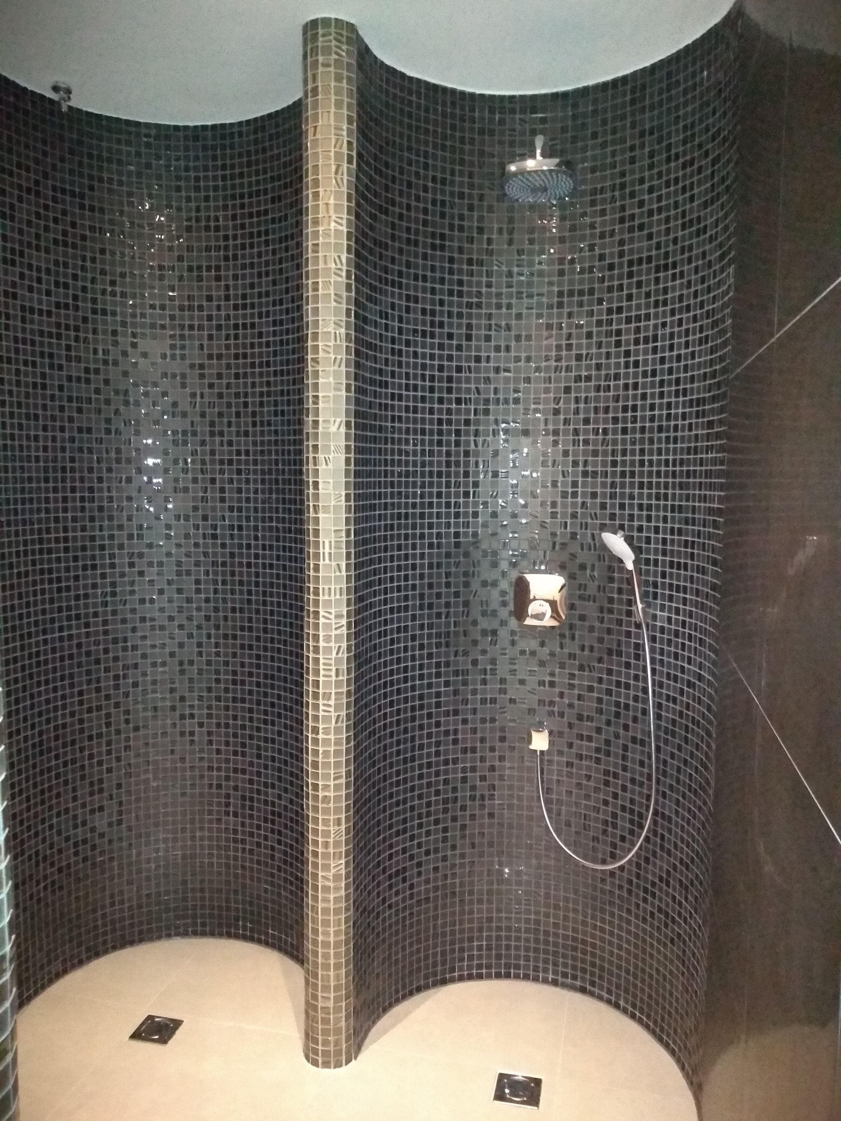 A shower with a curved design, tiled walls, and a handheld showerhead.