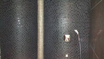 A shower with a curved design, tiled walls, and a handheld showerhead.