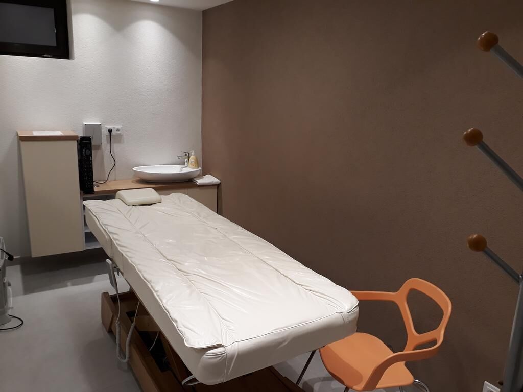 A small, private room with a single bed, a bedside table, a sink, and a chair.