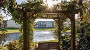 A wooden pergola with a bench overlooking a lake, surrounded by lush greenery. - Beautiful Lakeside Penthouse Award Winning Resort Just Minutes to Disney! (Kissimmee)