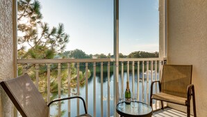 A balcony with a view of a lake, two chairs, a table with a bottle and glasses, and a string of lights. - Beautiful Lakeside Penthouse Award Winning Resort Just Minutes to Disney! (Kissimmee)