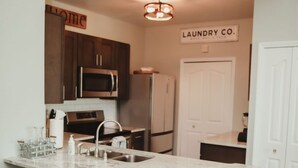 A kitchen with a marble countertop, dark wooden stools, a stainless steel sink, and a microwave. - Beautiful Lakeside Penthouse Award Winning Resort Just Minutes to Disney! (Kissimmee)