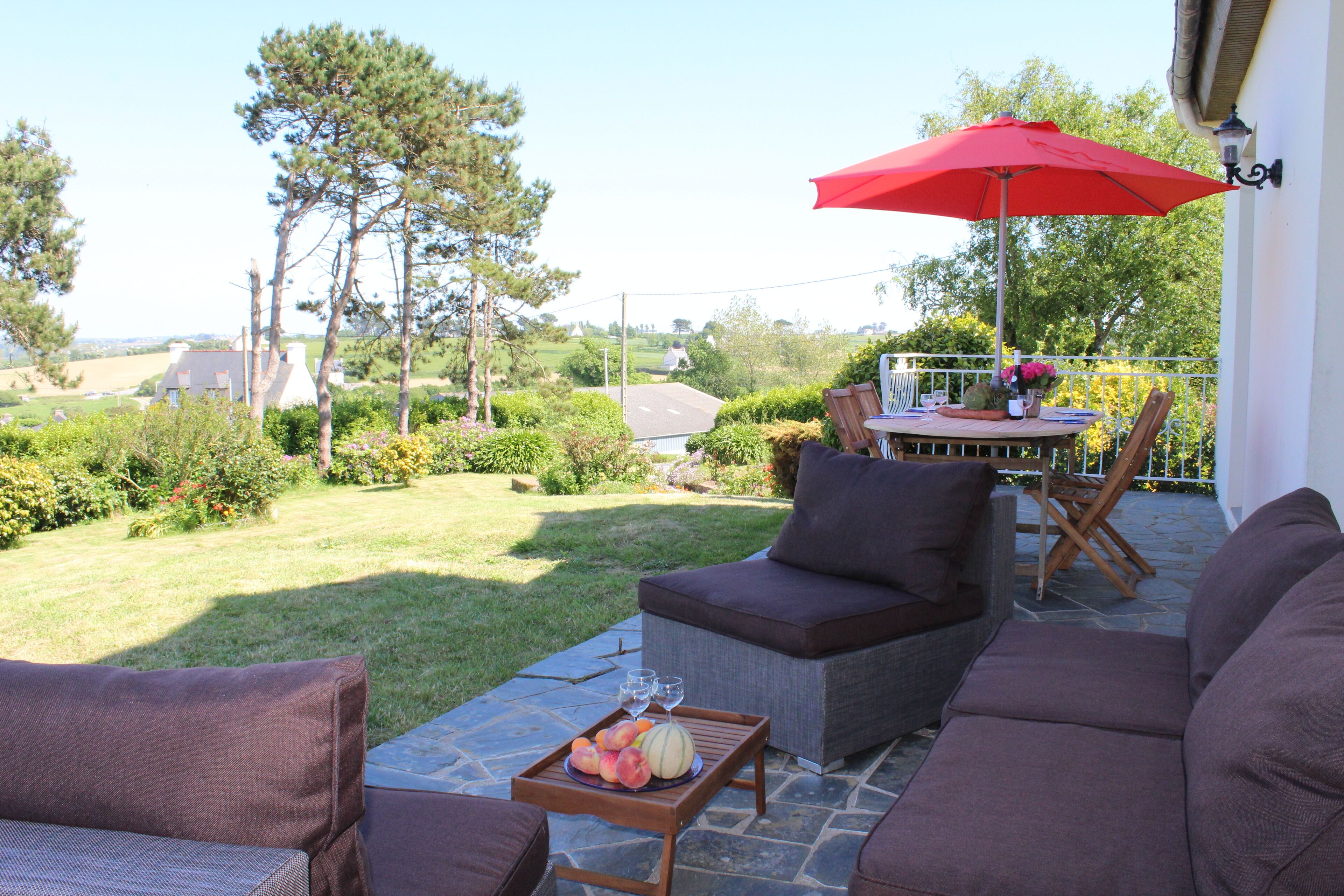 Une terrasse avec des meubles d’extérieur, une table à manger et un parasol rouge.