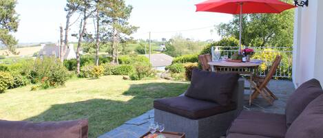 Une terrasse avec des meubles d’extérieur, une table à manger et un parasol rouge.