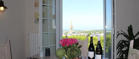 Uma mesa de jantar com vista para a torre de uma igreja, uma garrafa de vinho e um vaso de flores.