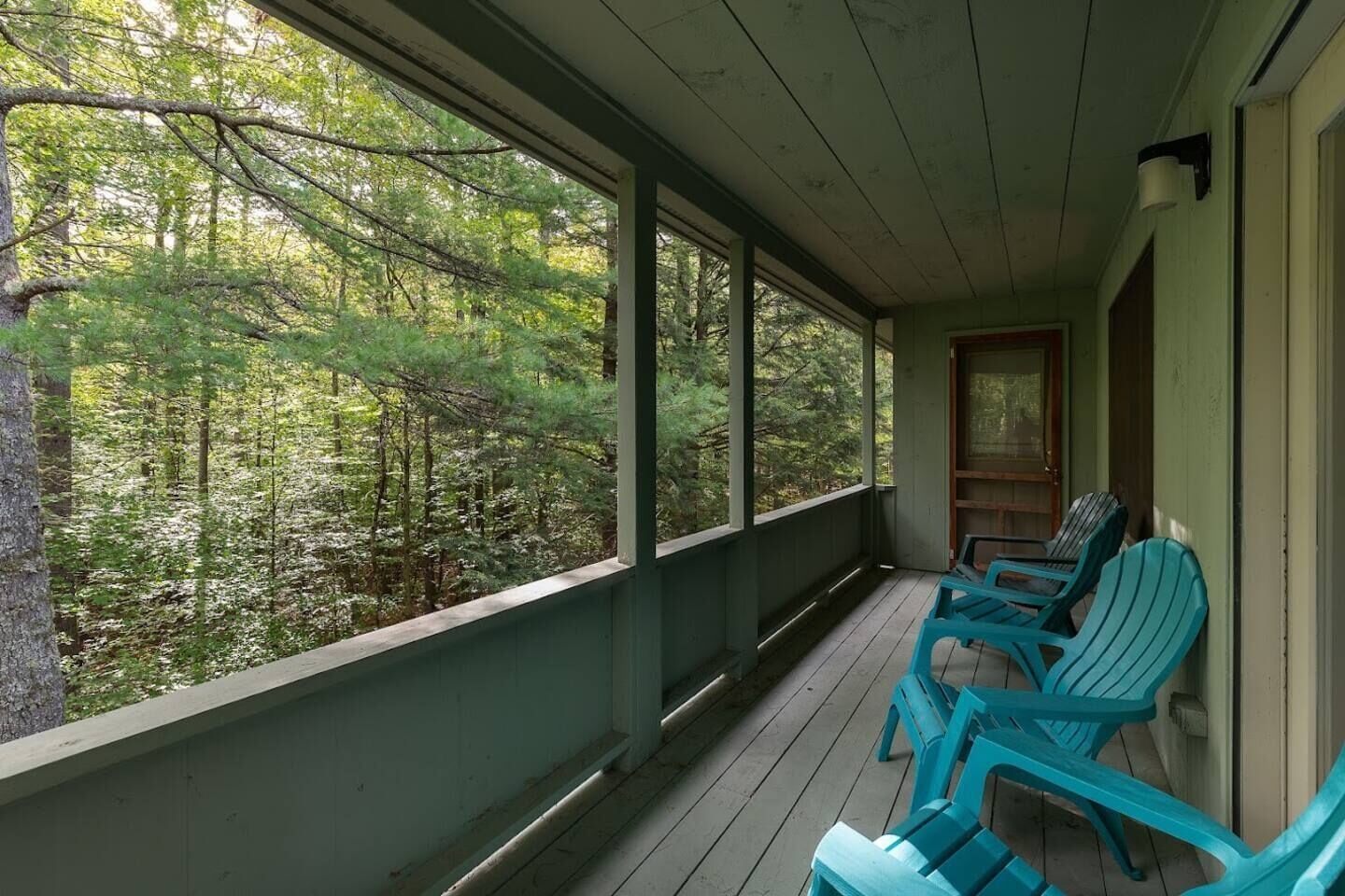 A porch with a view of a forest. There are three chairs and a table.