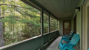 A porch with a view of a forest. There are three chairs and a table. - Great place to stay for multiple families all year (Bartlett)