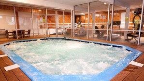 A hot tub with a wooden deck surrounding it, indoor seating area with tables and chairs, and a view through glass doors to an outdoor space with exercise equipment. - Great place to stay for multiple families all year (Bartlett)