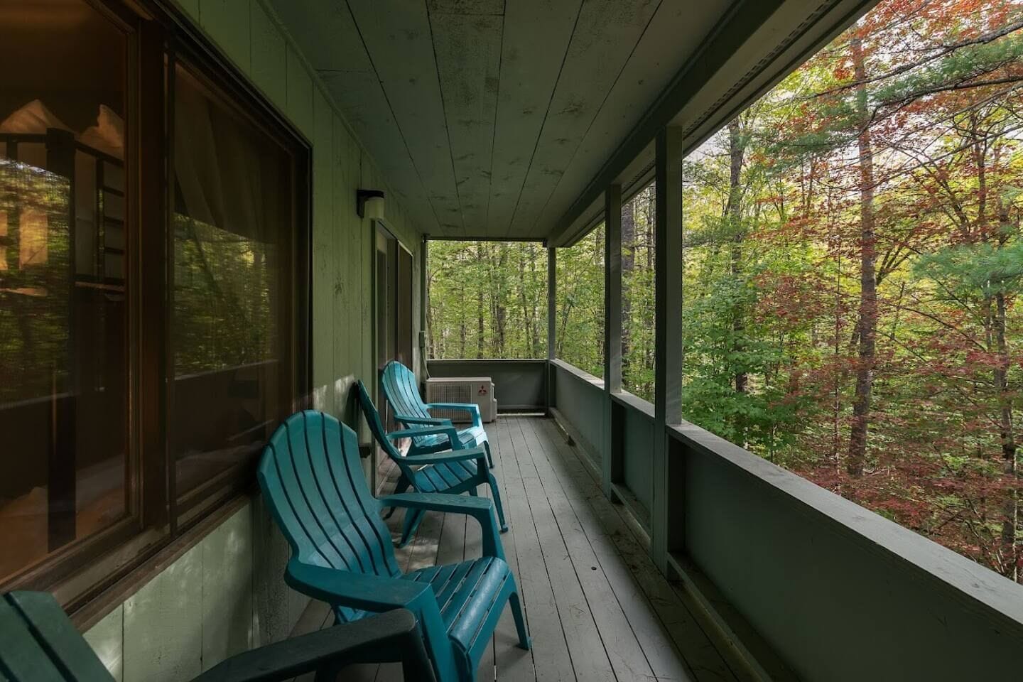 Un porche techado con piso de madera y sillas Adirondack verdes.