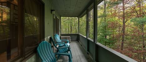Un porche techado con piso de madera y sillas Adirondack verdes.