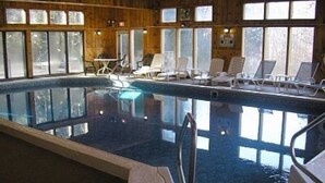 An indoor swimming pool with clear glass walls, lounge chairs, and wooden paneling. - Great place to stay for multiple families all year (Bartlett)