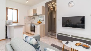 Una cuina moderna amb microones, forn i rentamics, una zona de estar amb sofà i televisió, i una zona de dinar amb taula i bols de llaminades.