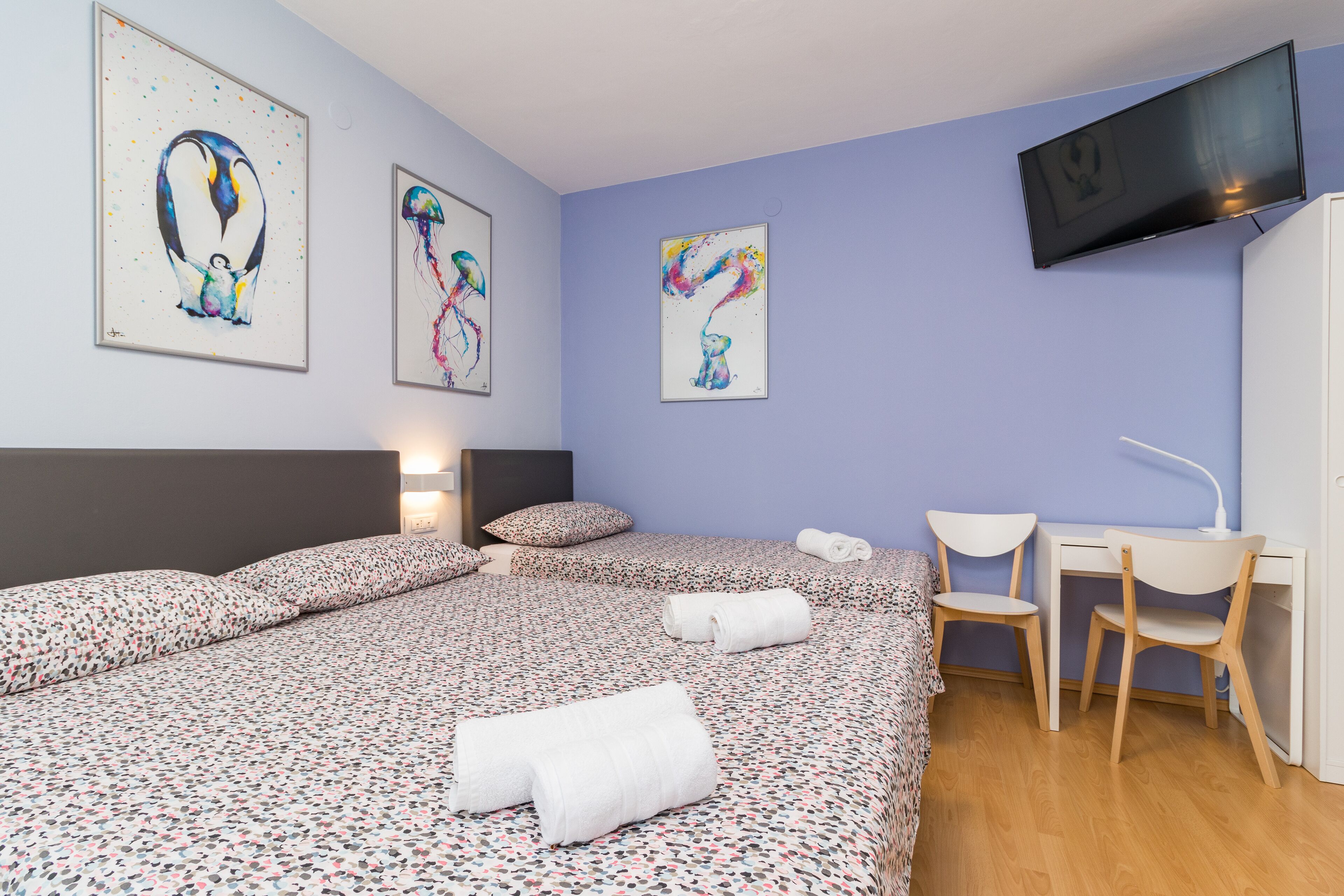 Une chambre d’hôtel avec un grand lit, deux tables de chevet, un bureau avec une chaise et des œuvres d’art accrochées aux murs.