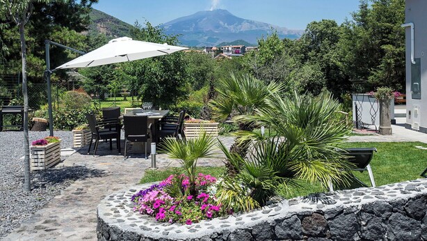 An outdoor patio with a table and chairs, surrounded by a stone wall and potted plants. - Luxury villa with pool on the slopes of Etna (Nicolosi)